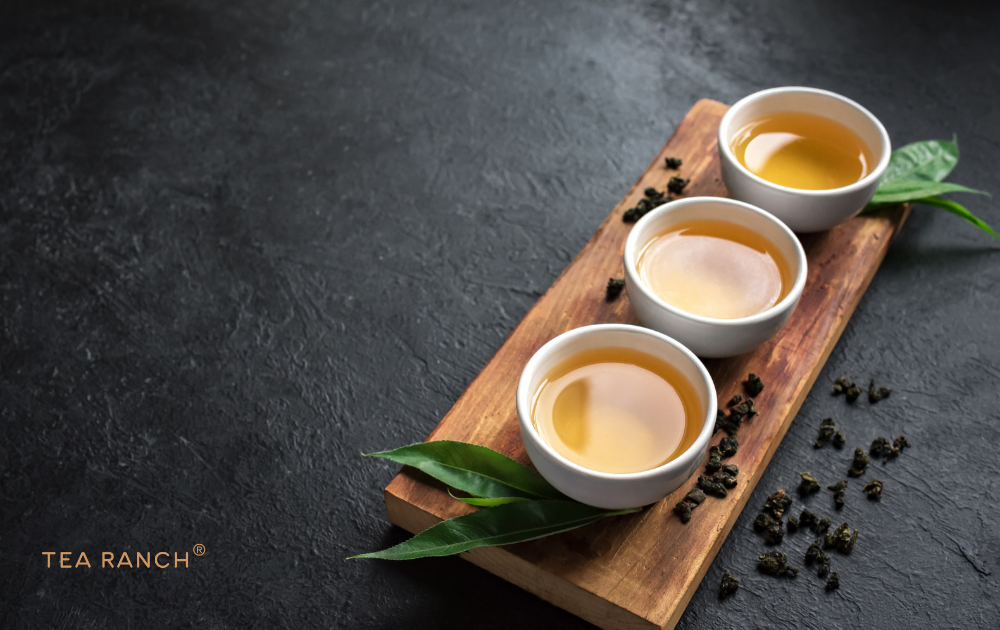 Oolong Tea Can Range from Light Golden to Rich Amber Three cups of oolong tea showing different golden amber hues alongside rolled oolong tea leaves, illustrating the wide range of flavors and oxidation levels found in oolong tea.