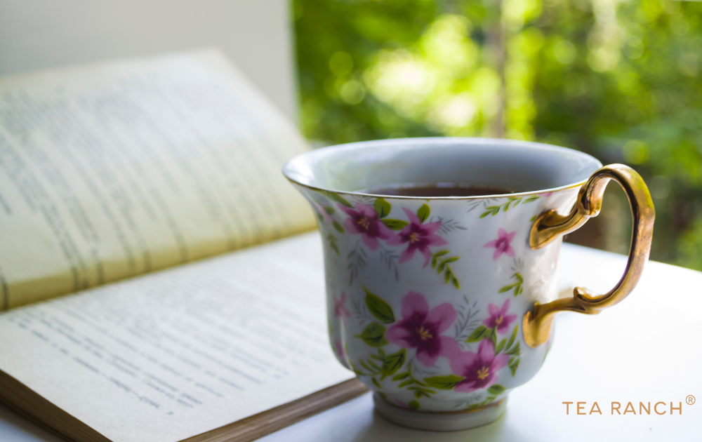 Floral teacup beside an open book near a sunny window, creating a peaceful moment for relaxation, reading, and mindful tea drinking.